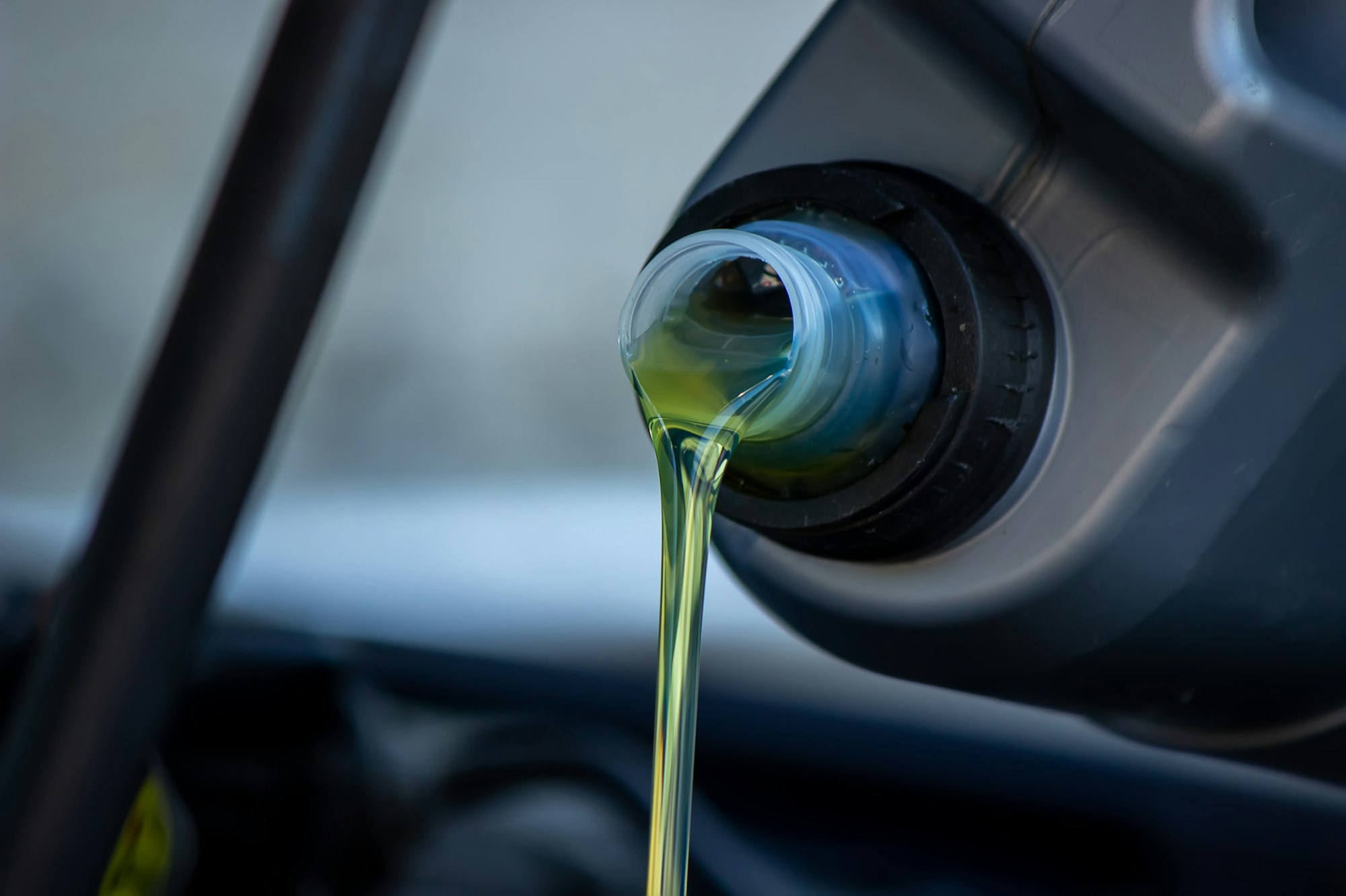 An auto mechanic changing oil pours oil into a car engine.